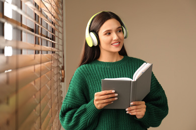 Young woman listening to audiobook near window indoors