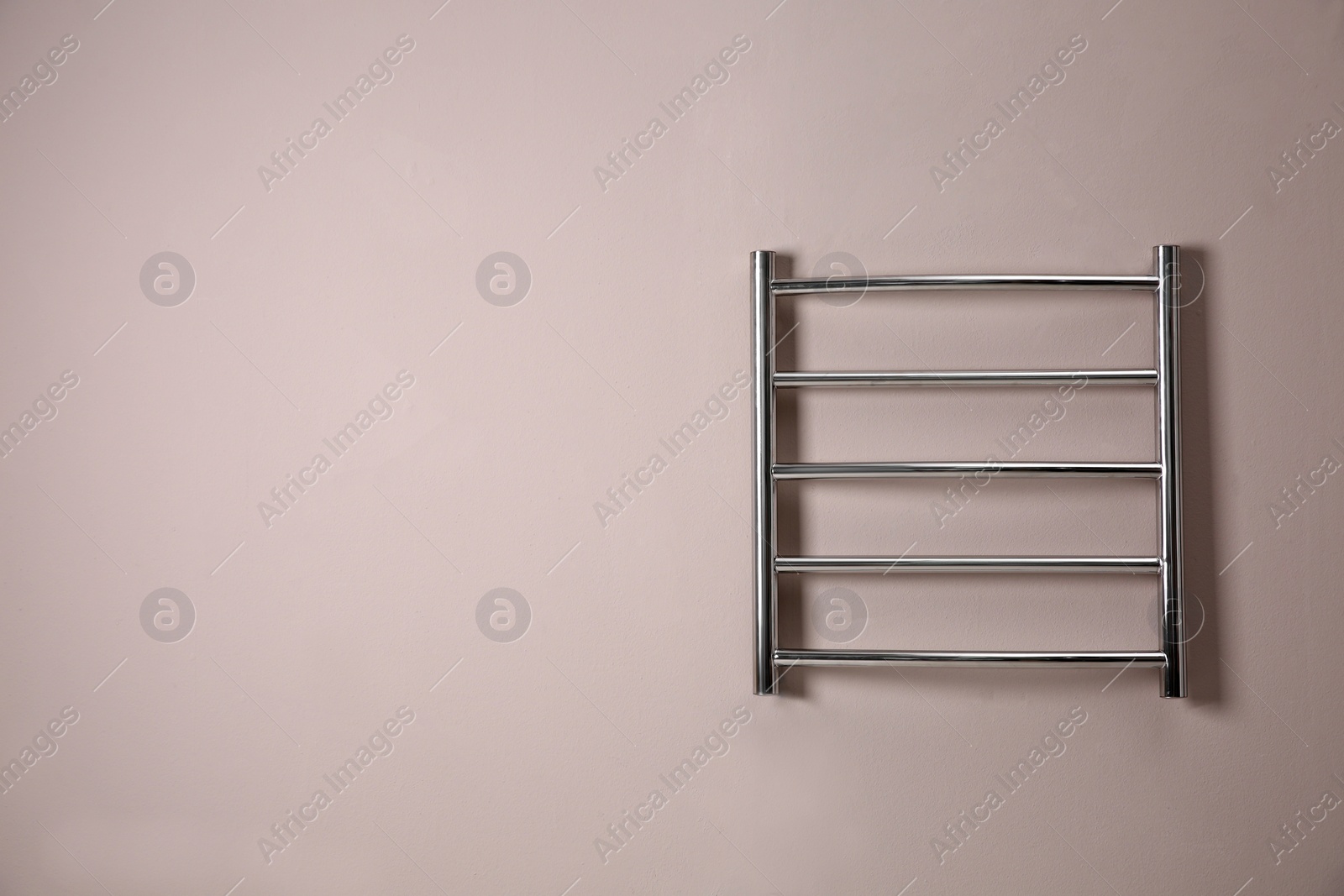 Photo of Modern heated towel rail on light wall. Space for text