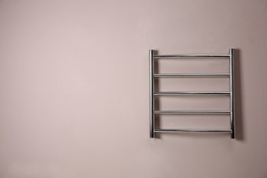 Modern heated towel rail on light wall. Space for text