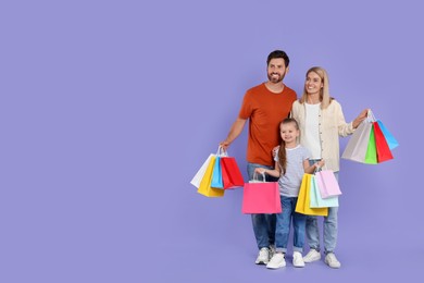 Photo of Family shopping. Happy parents and daughter with many colorful bags on violet background. Space for text