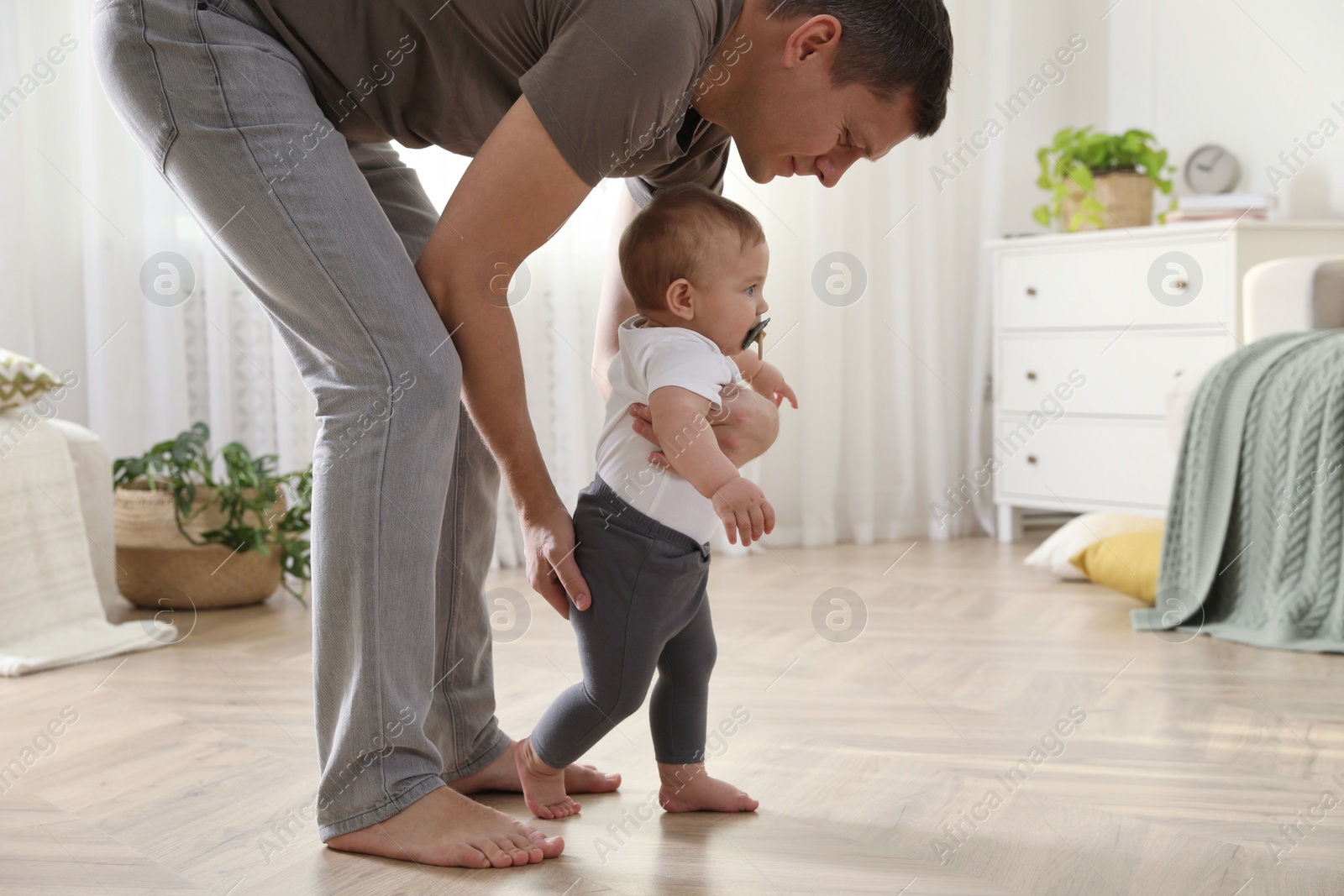 Photo of Father supporting his baby daughter while she learning to walk at home