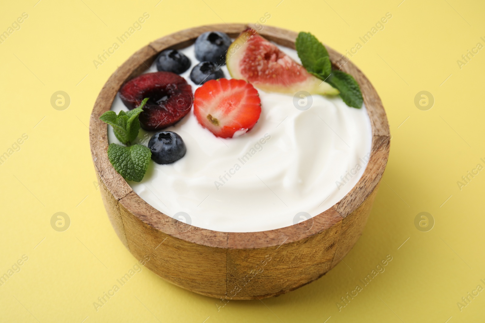 Photo of Bowl with yogurt, berries, fruits and mint on yellow background, closeup