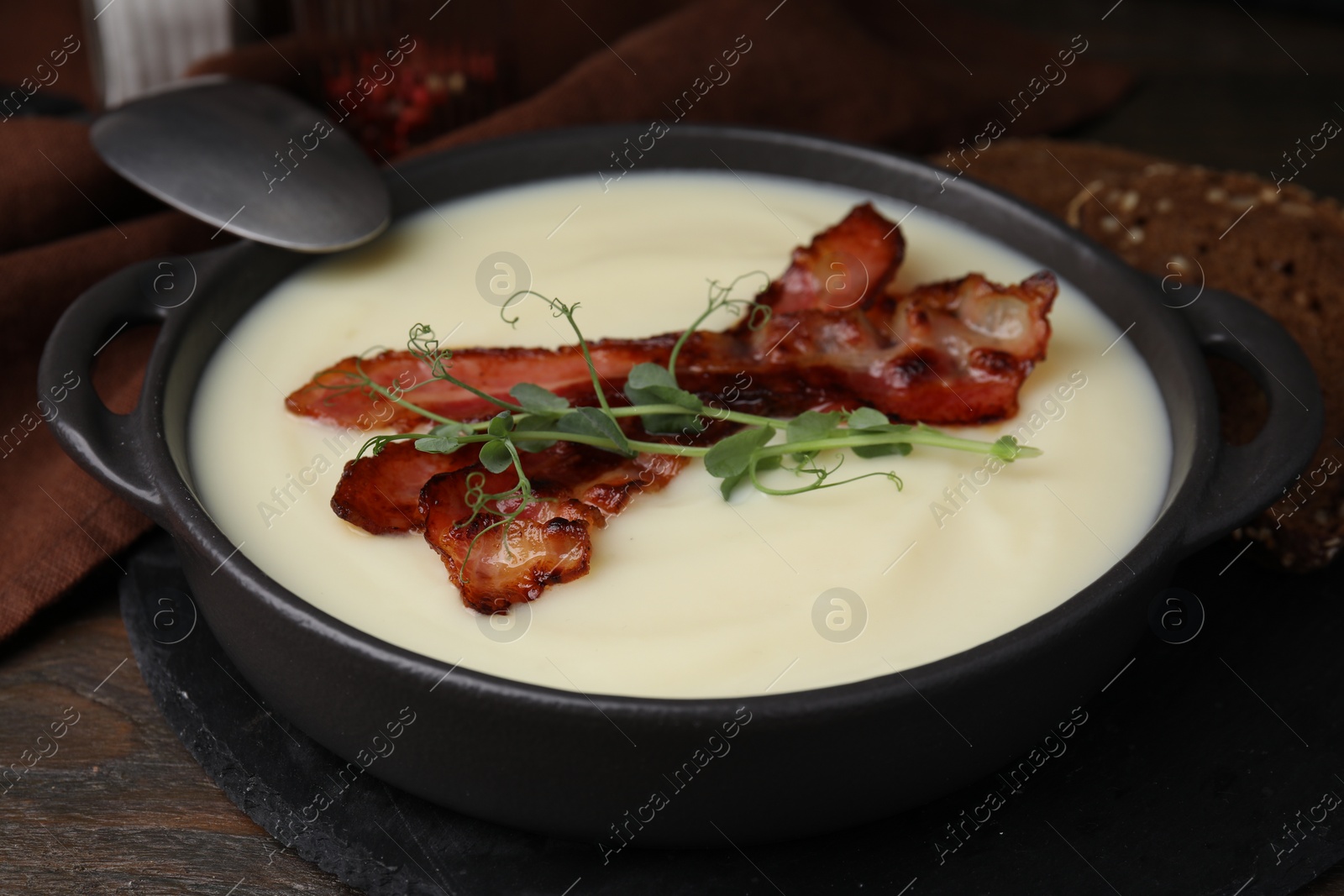 Photo of Delicious potato soup with bacon and microgreens in bowl served on wooden table, closeup