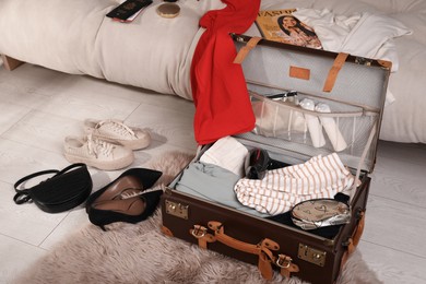 Photo of Open suitcase with clothes, accessories and shoes in living room