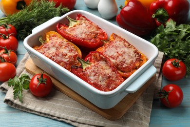 Photo of Tasty stuffed peppers in dish and ingredients on light blue wooden table