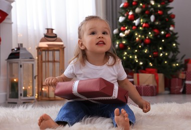 Photo of Cute little girl with Christmas gift in festively decorated room