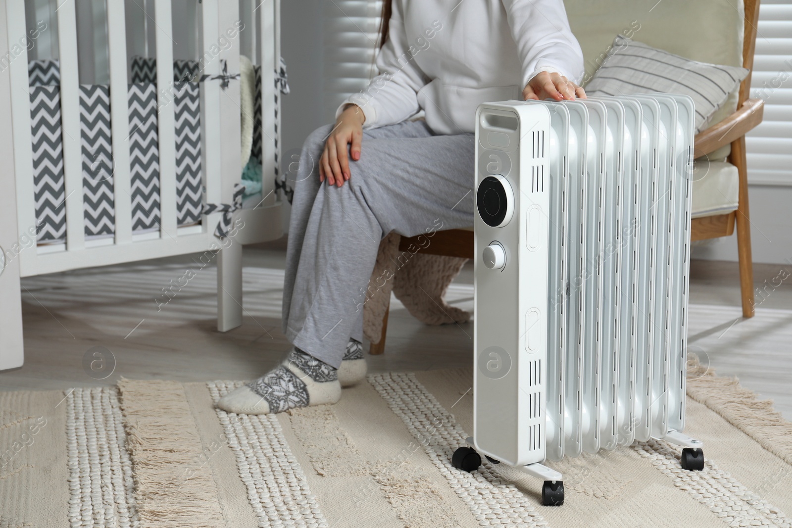 Photo of Young woman adjusting temperature on modern electric heater in child room, closeup