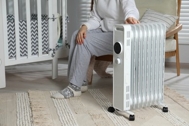 Photo of Young woman adjusting temperature on modern electric heater in child room, closeup