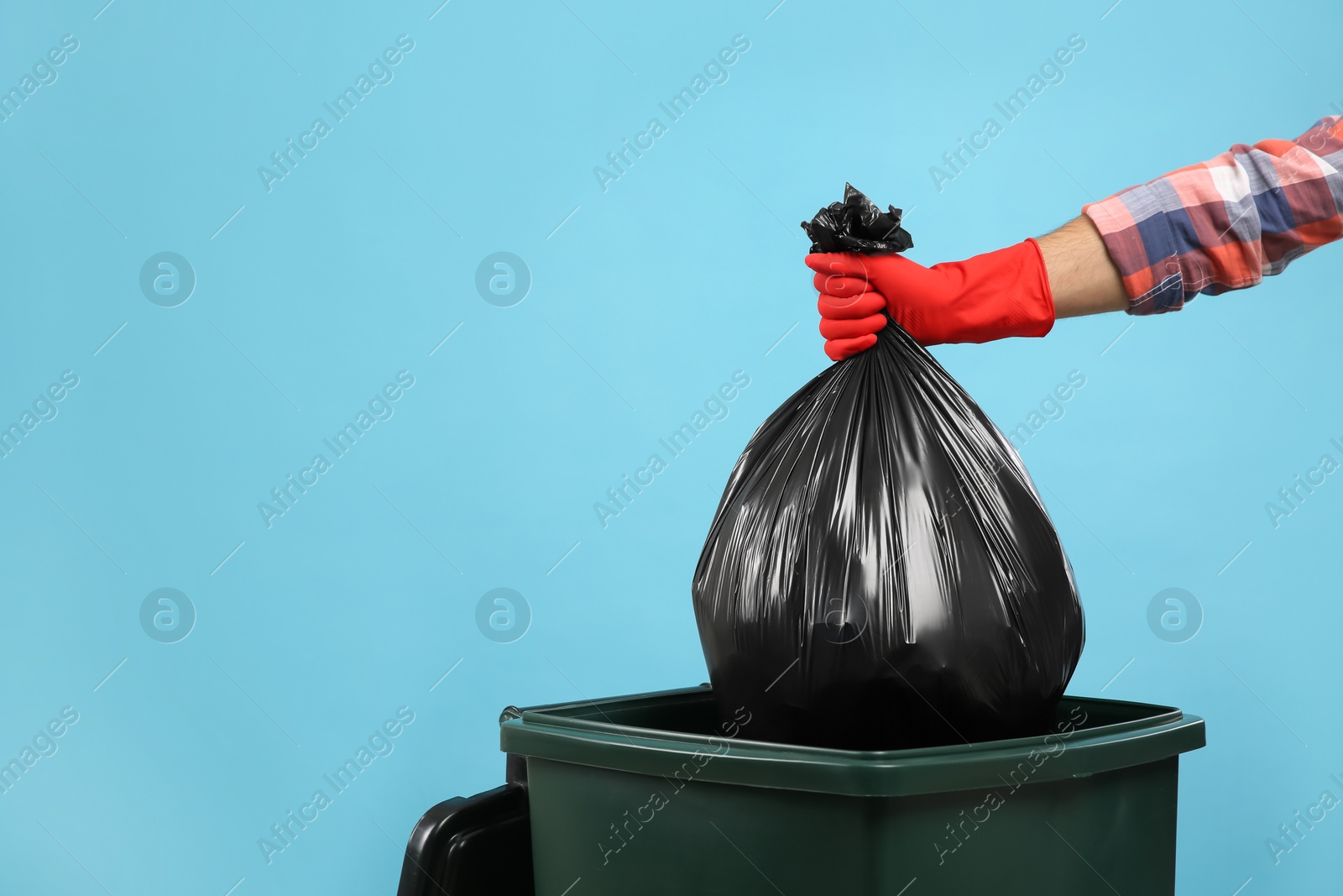 Photo of Man throwing garbage bag into bin on light blue background, closeup. Space for text