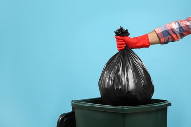 Photo of Man throwing garbage bag into bin on light blue background, closeup. Space for text