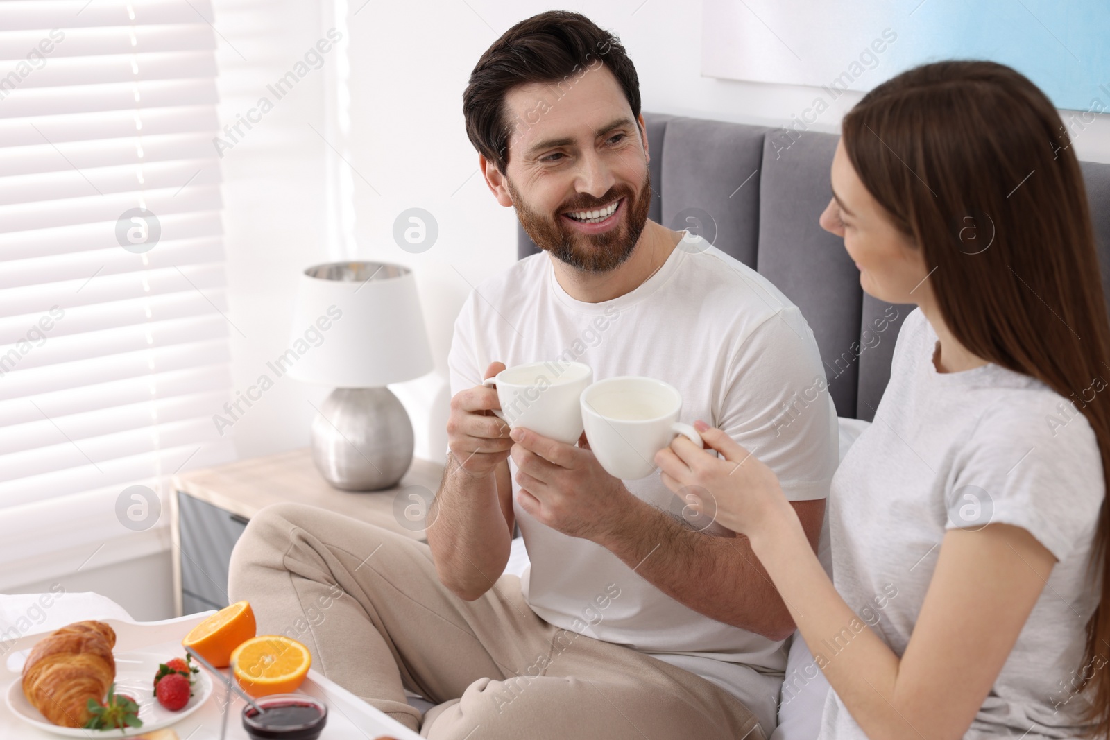 Photo of Happy couple eating tasty breakfast on bed at home