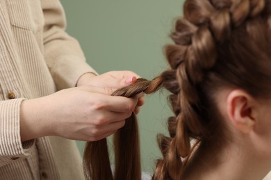 Photo of Professional stylist braiding woman's hair on olive background, closeup