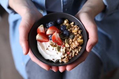 Woman holding bowl of tasty granola with berries, yogurt and seeds, top view