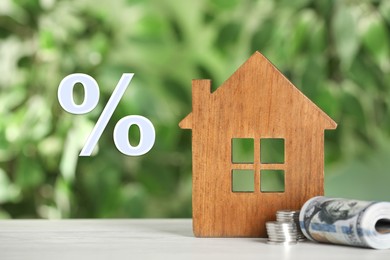 Image of Mortgage. Wooden house model, money and percent sign on blurred green background