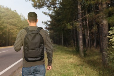Man with backpack on road near forest, back view