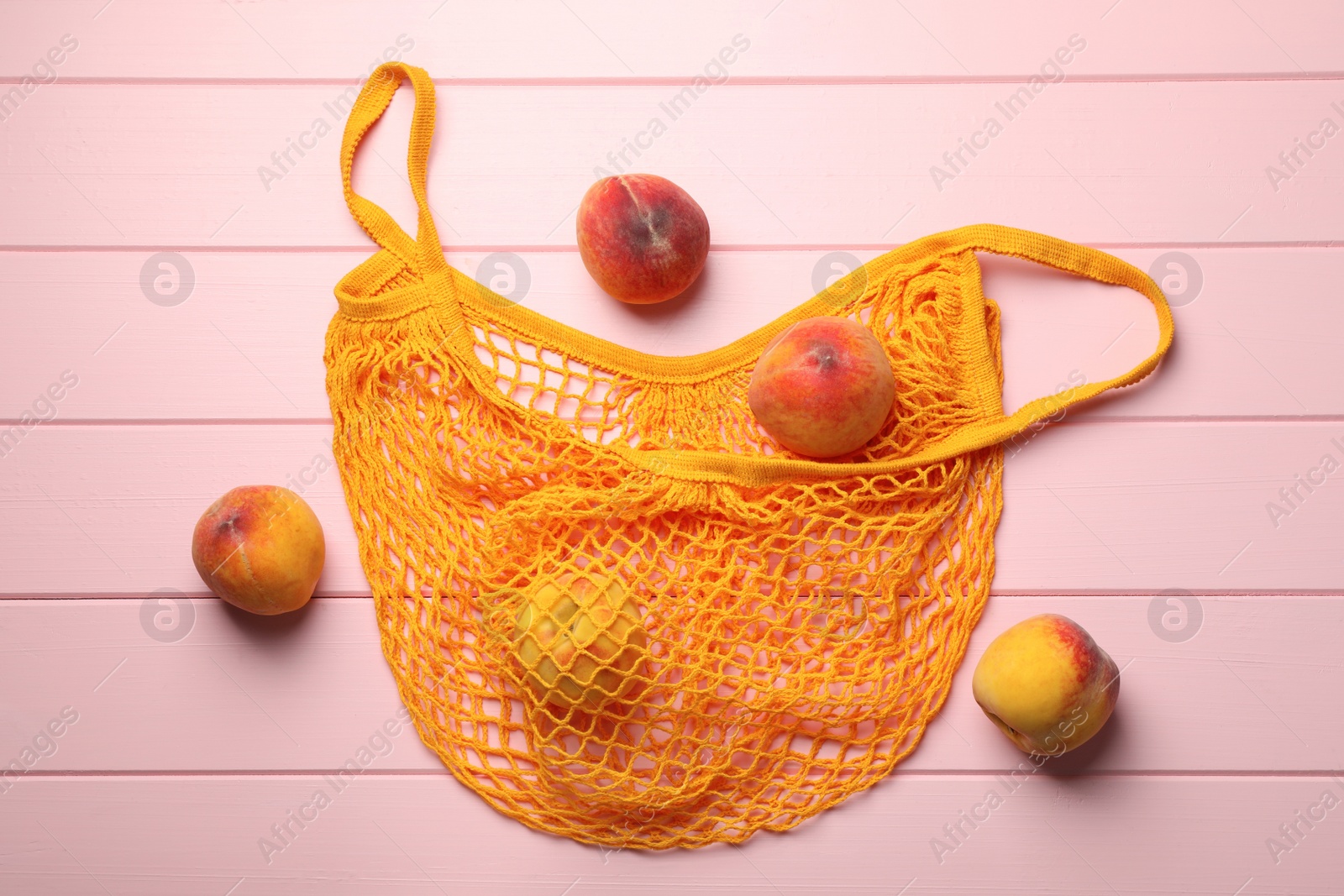 Photo of Net bag with fresh ripe peaches on pink wooden table, flat lay