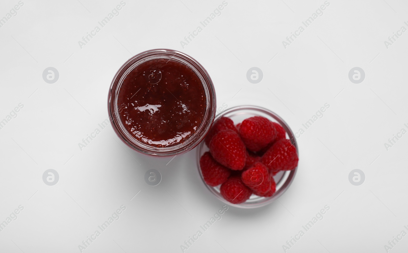 Photo of Tasty canned raspberry jam and fresh berries on white background, top view