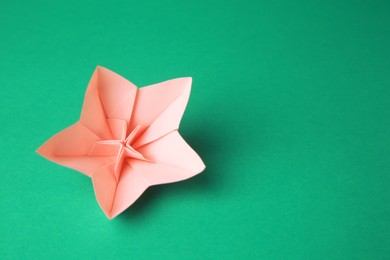 Origami art. Handmade pink paper flower on green background, above view with space for text