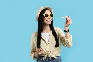 Happy female tourist with toy plane on light blue background