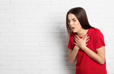 Photo of Beautiful young woman coughing near brick wall. Space for text