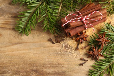 Different spices and fir branches on wooden table, flat lay. Space for text