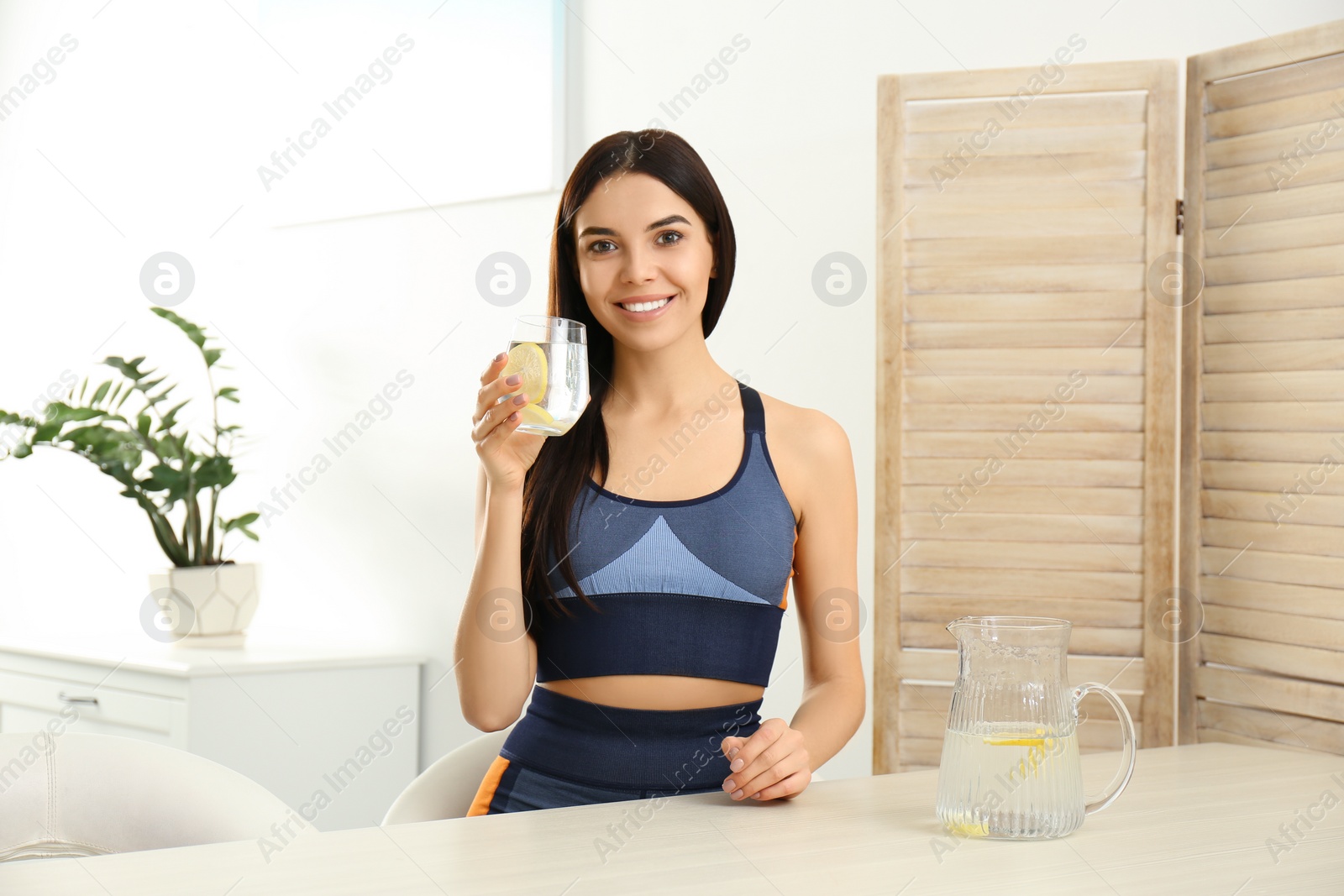 Photo of Beautiful sportive woman with lemon water at table indoors