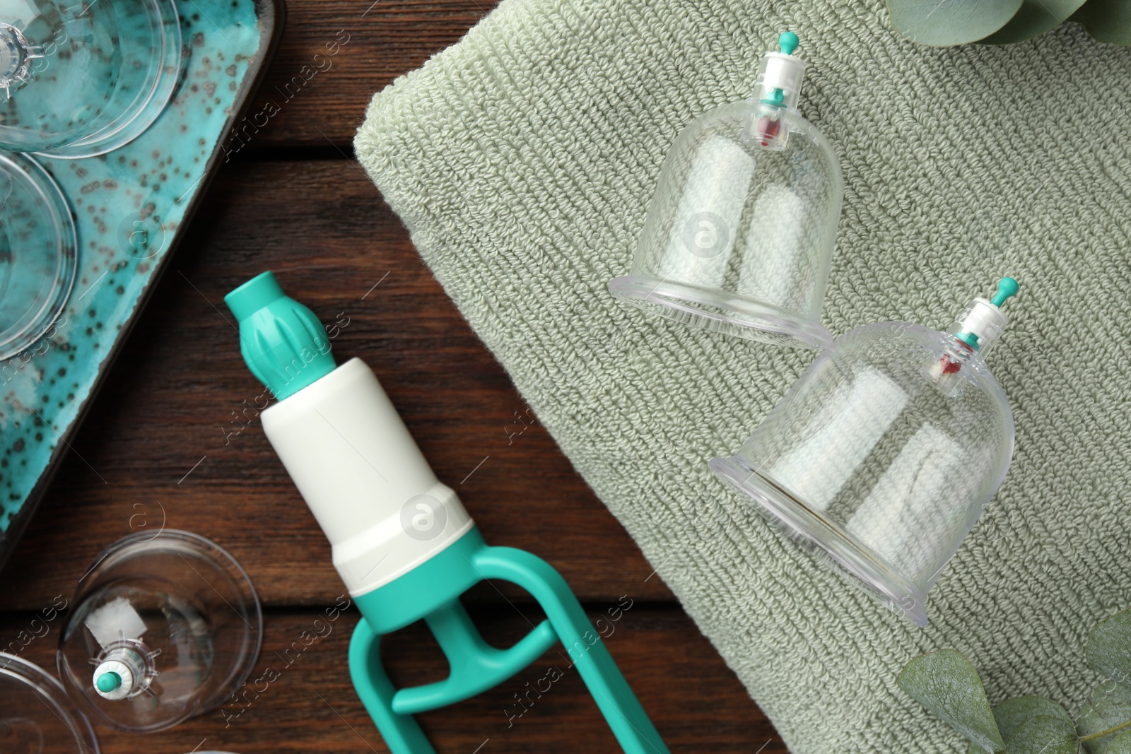 Photo of Cupping therapy. Plastic cups, hand pump and towel on wooden table, flat lay