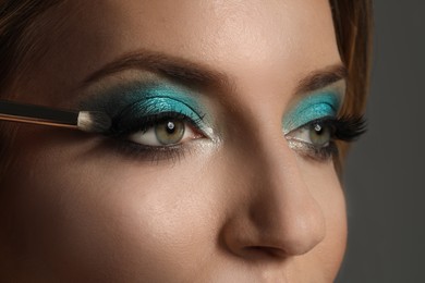Photo of Applying eye shadow onto woman's face on grey background, closeup. Beautiful evening makeup