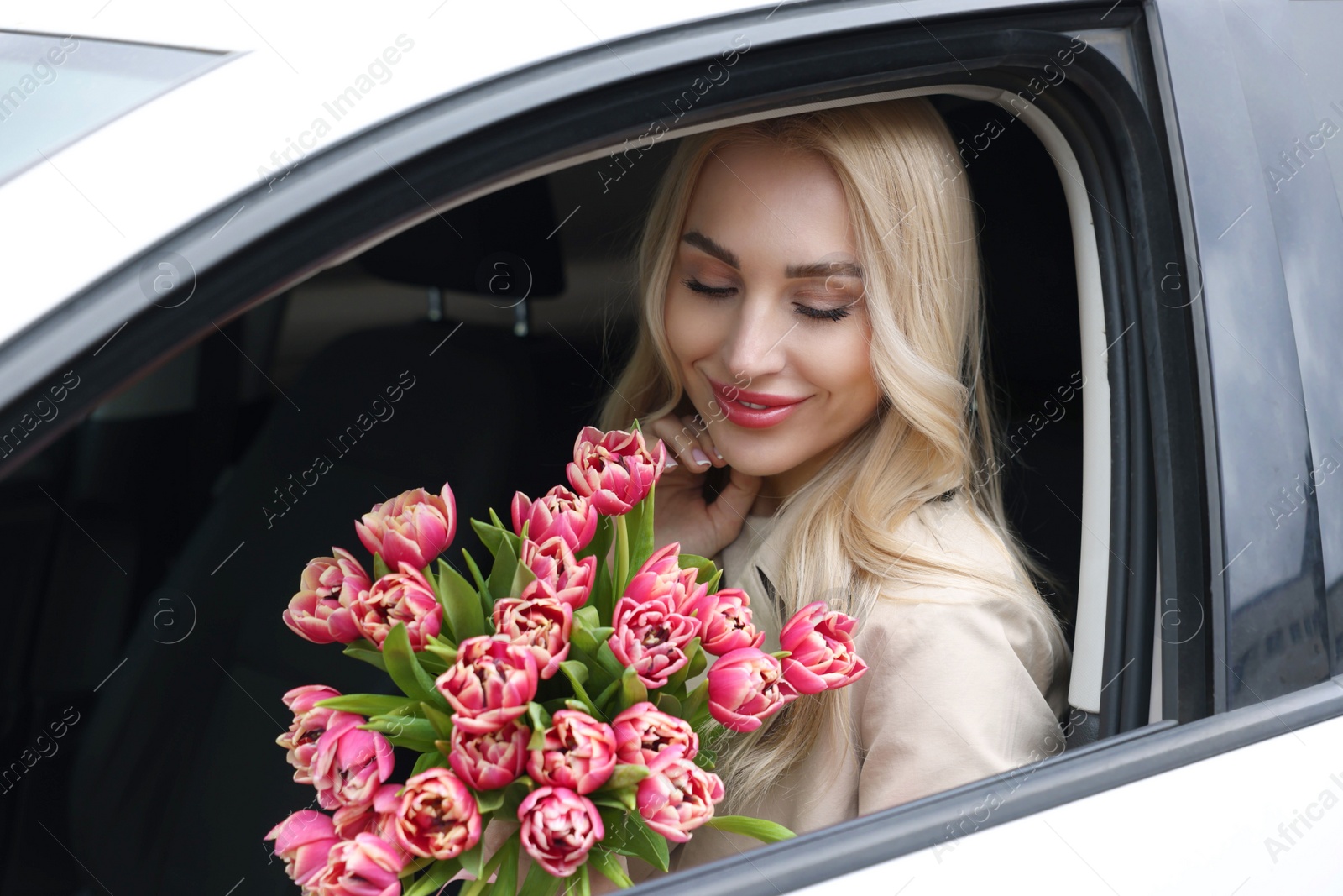 Photo of Happy young woman with beautiful bouquet in car