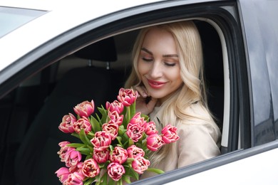 Happy young woman with beautiful bouquet in car