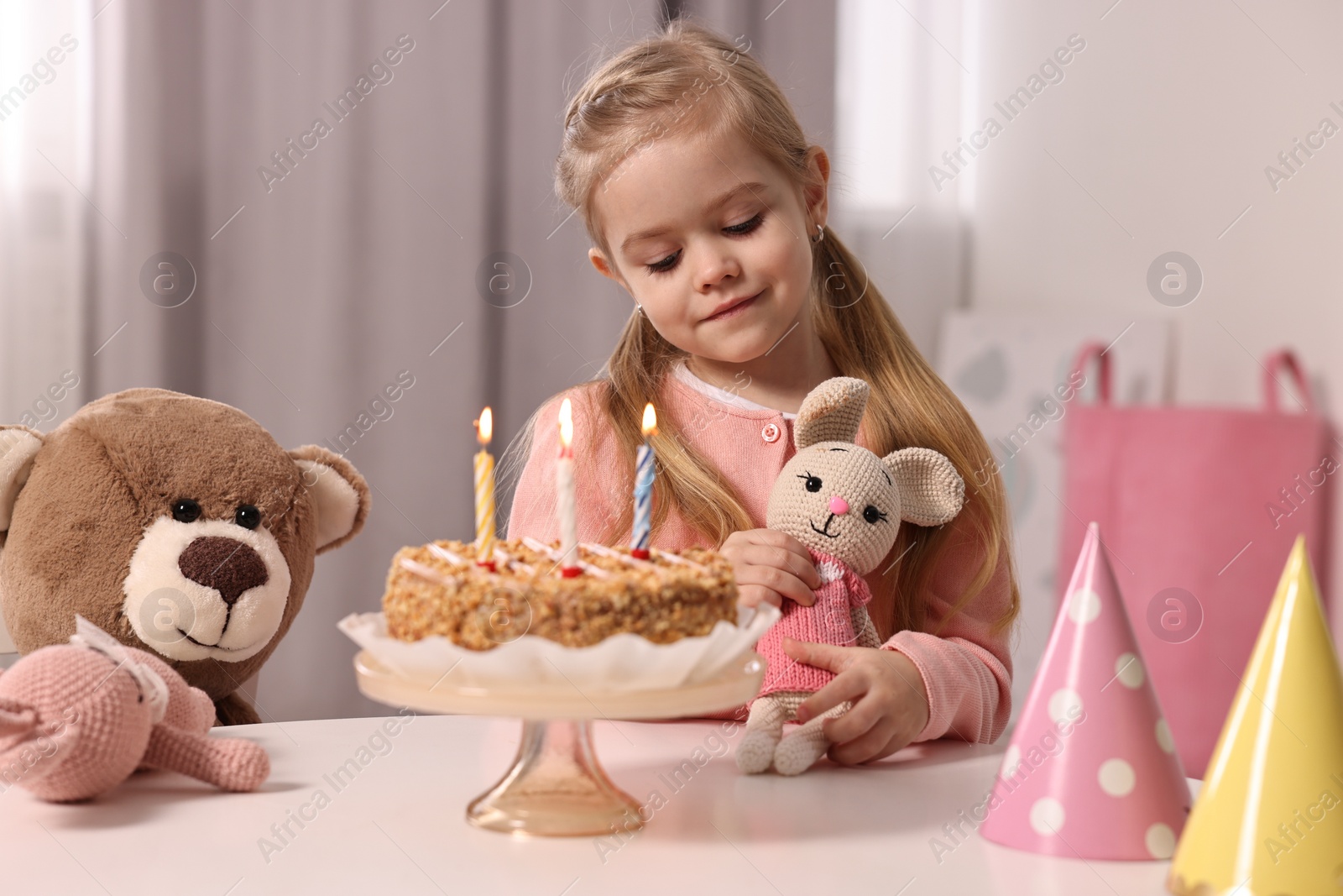 Photo of Cute girl with birthday cake and toys at table indoors