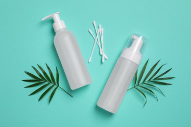 Different cleansers, cotton buds and leaves on turquoise background, flat lay with space for text. Cosmetic product