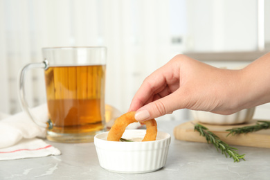 Photo of Woman dipping crunchy fried onion ring in sauce at grey marble table, closeup