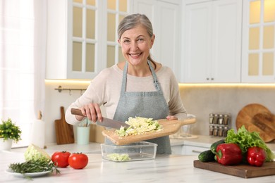 Happy housewife putting cut cabbage into glass container at white marble table in kitchen