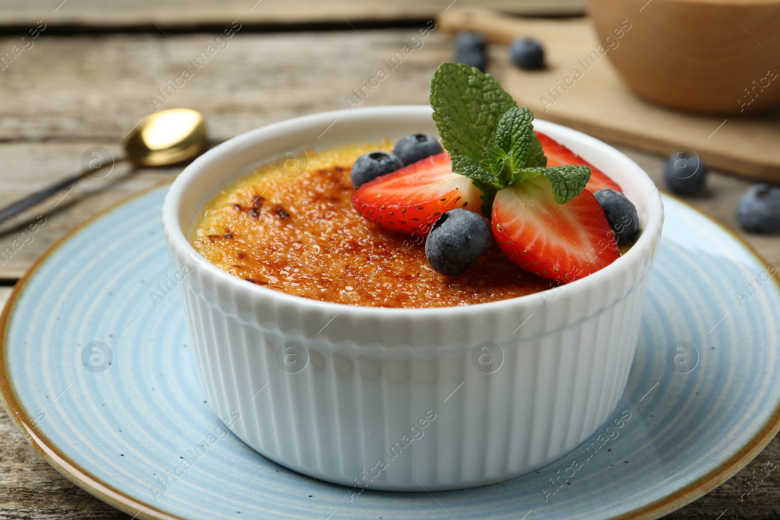 Photo of Delicious creme brulee with berries and mint in bowl on wooden table, closeup