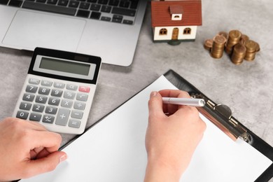Photo of Woman planning budget, closeup. House model, calculator and coins on grey table