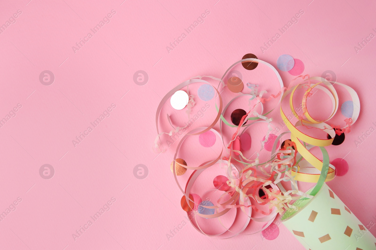 Photo of Beautiful serpentine and confetti bursting out of party popper on pink background, flat lay. Space for text