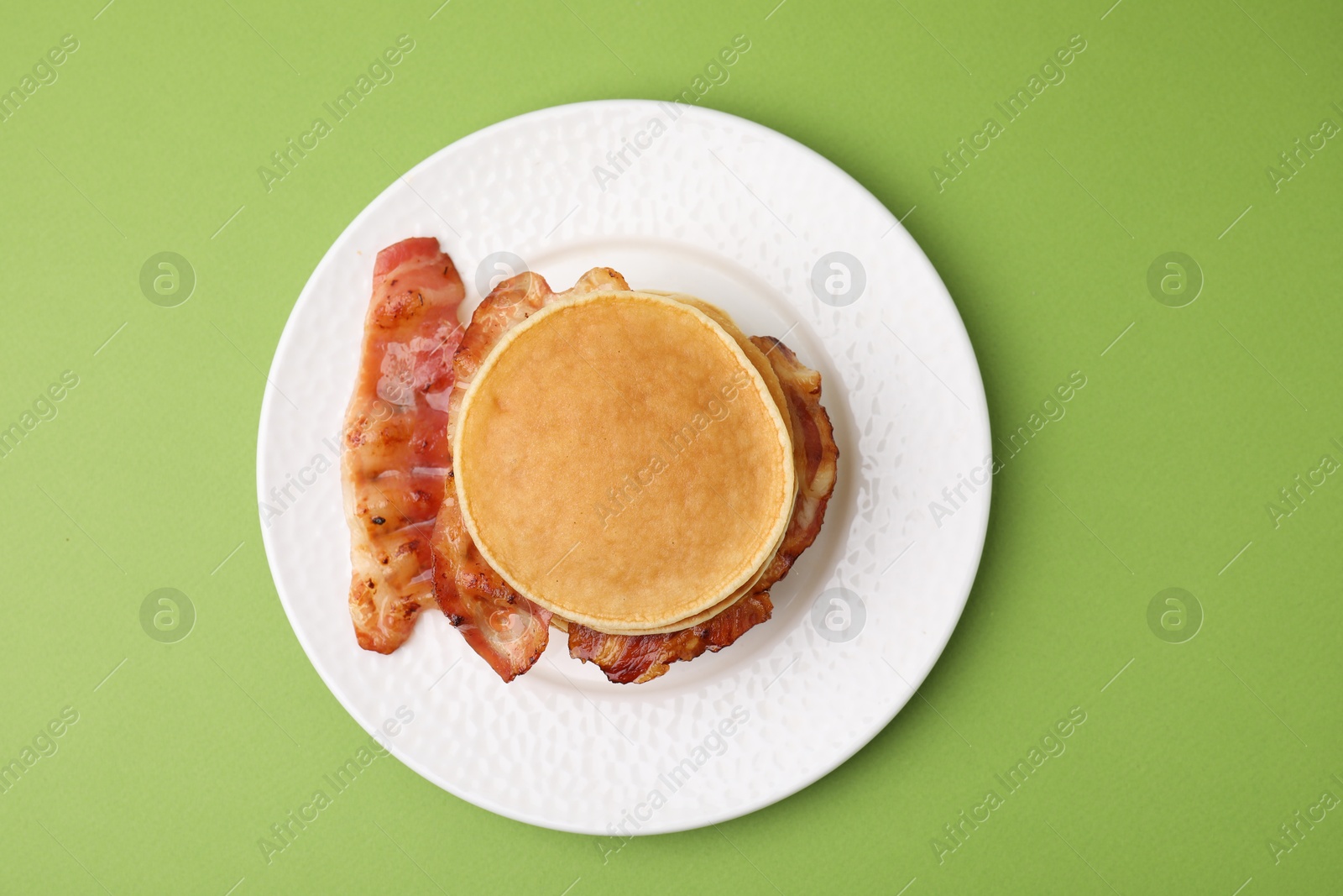 Photo of Delicious pancakes with bacon on green table, top view