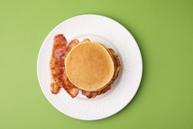 Delicious pancakes with bacon on green table, top view