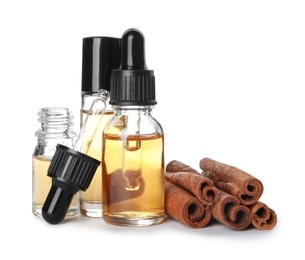 Photo of Bottles of essential oils and cinnamon sticks on white background