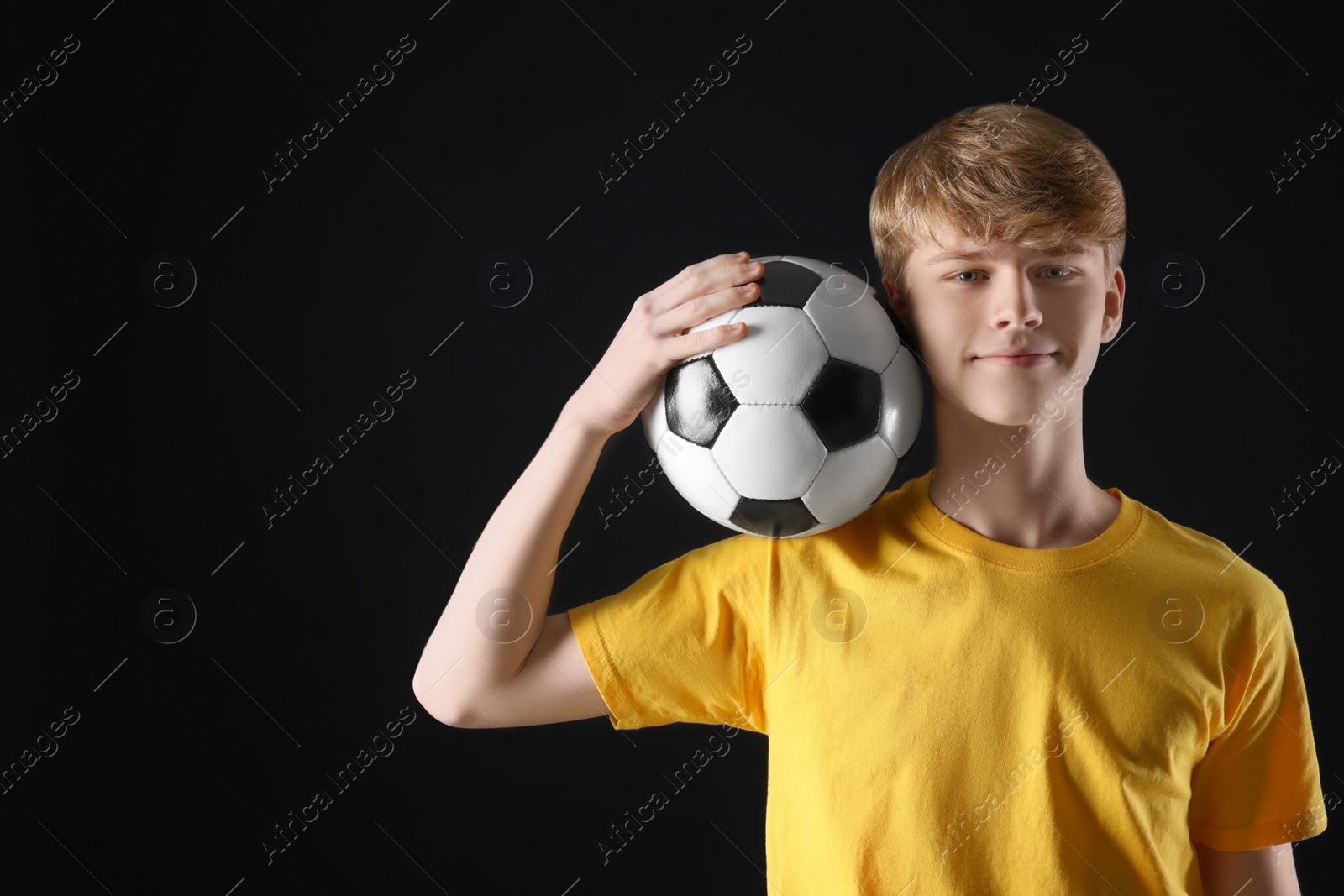 Photo of Teenage boy with soccer ball on black background. Space for text