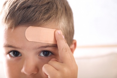 Photo of Little boy with adhesive bandage on forehead indoors, closeup