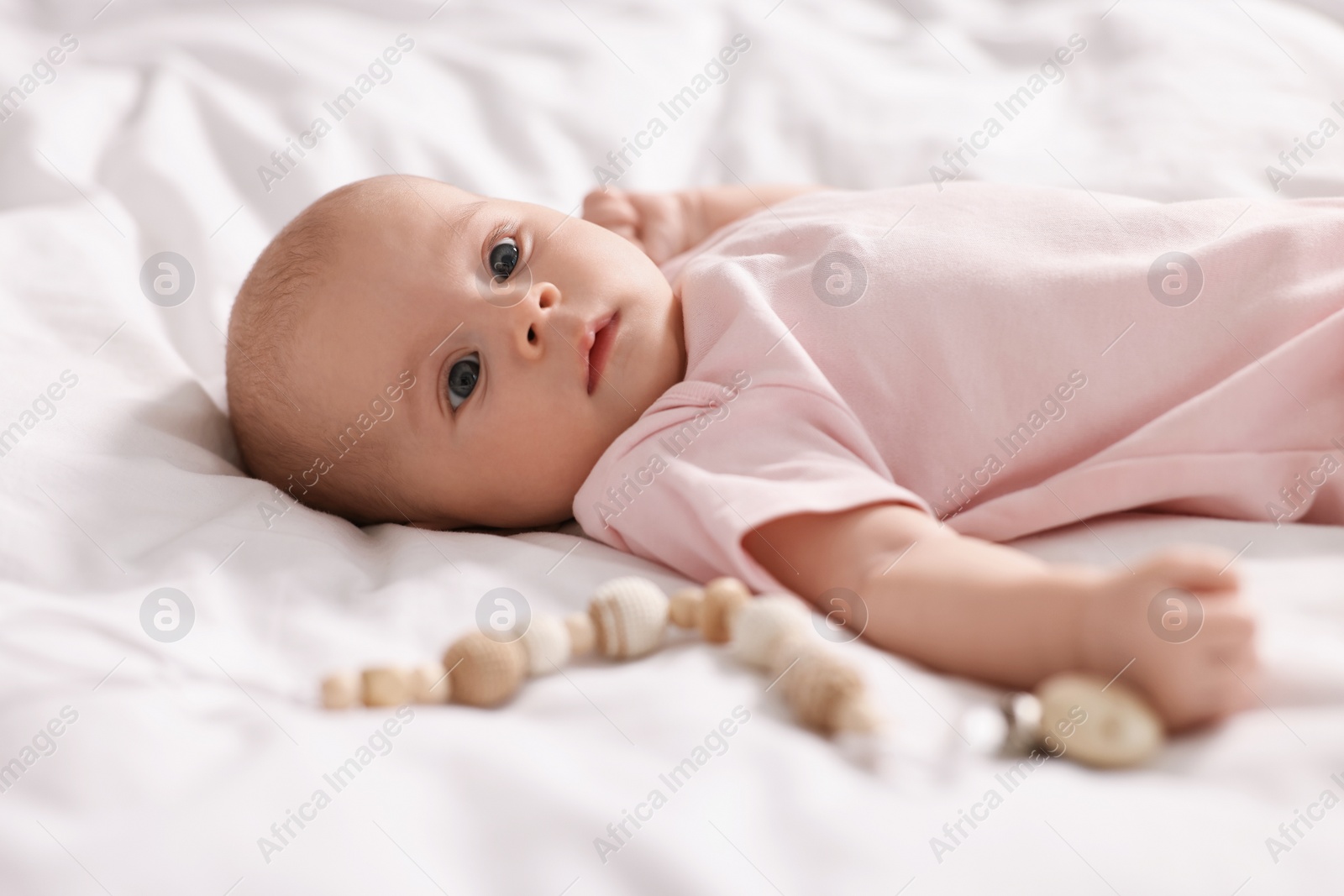 Photo of Cute little baby with toy lying on white sheets