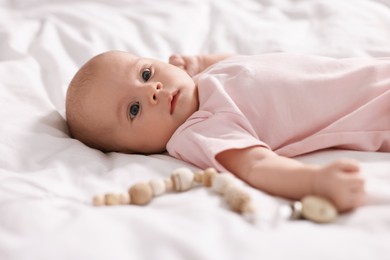 Photo of Cute little baby with toy lying on white sheets