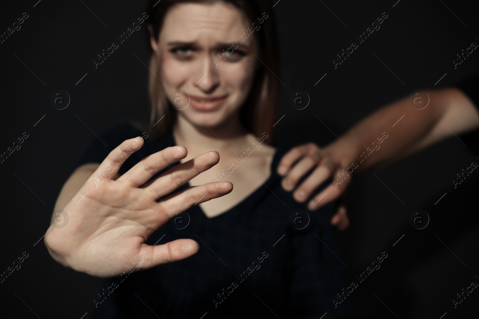 Photo of Man grabbing young woman with outstretched hand on dark background, closeup. Stop sexual assault