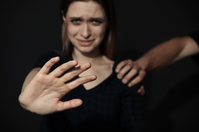 Photo of Man grabbing young woman with outstretched hand on dark background, closeup. Stop sexual assault