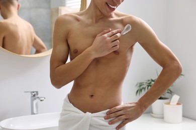 Man applying moisturizing cream onto his shoulder in bathroom, closeup