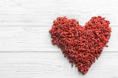 Photo of Heart made of dried goji berries on white wooden table, top view with space for text. Healthy superfood