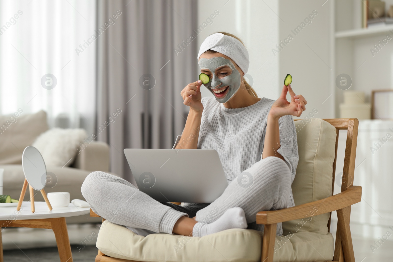 Photo of Young woman with face mask and cucumber slices using laptop at home. Spa treatments