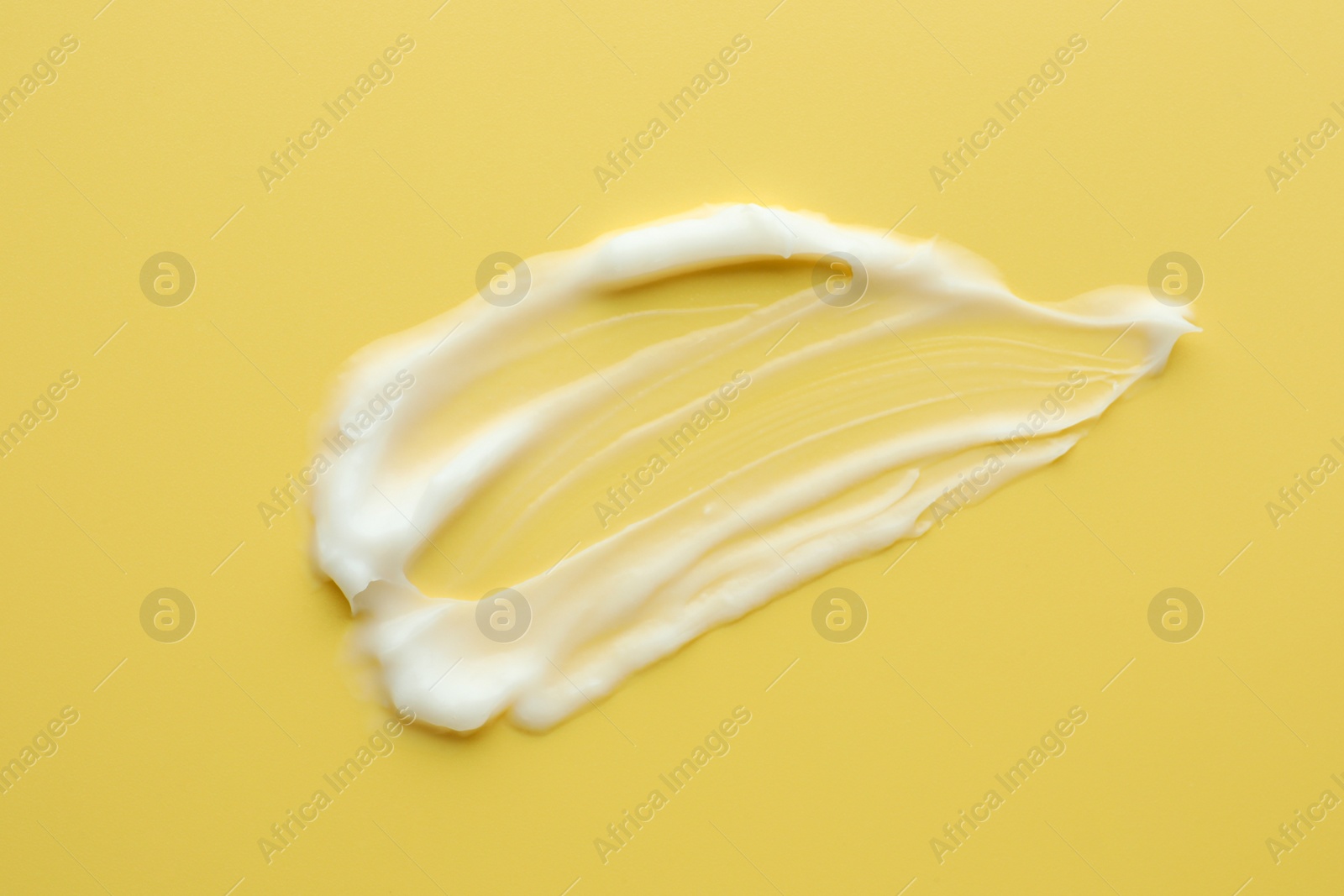 Photo of Sample of face cream on yellow background, top view